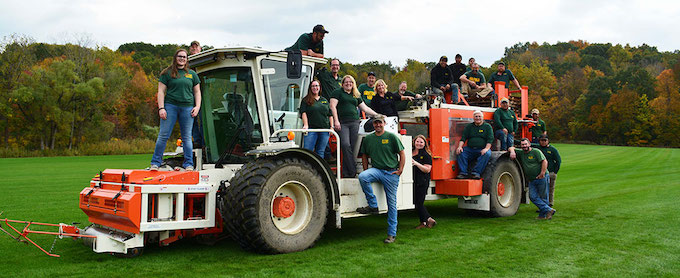 The Saratoga Sod team posing on a sod harvester for a photo.